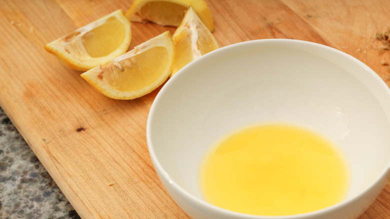 A bowl full of melted butter with lemon wedges on the side