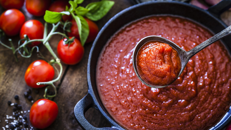 Marinara sauce in a skillet with a ladle and tomatoes on the side