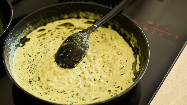 Creamy pesto sauce simmering in a pan with a spoon