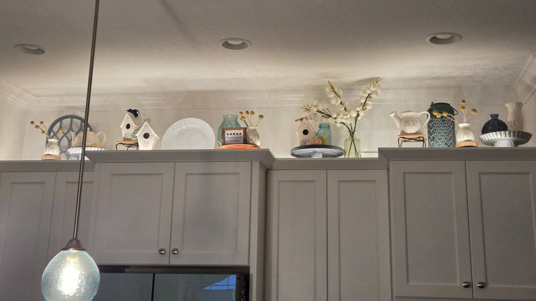 Dishes and decor in lighted area above kitchen cabinets