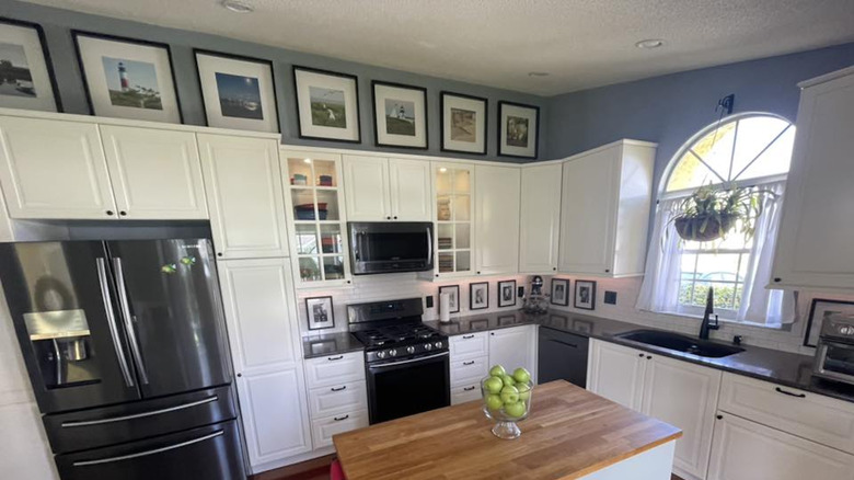 Framed photos of scenery above white kitchen cabinets