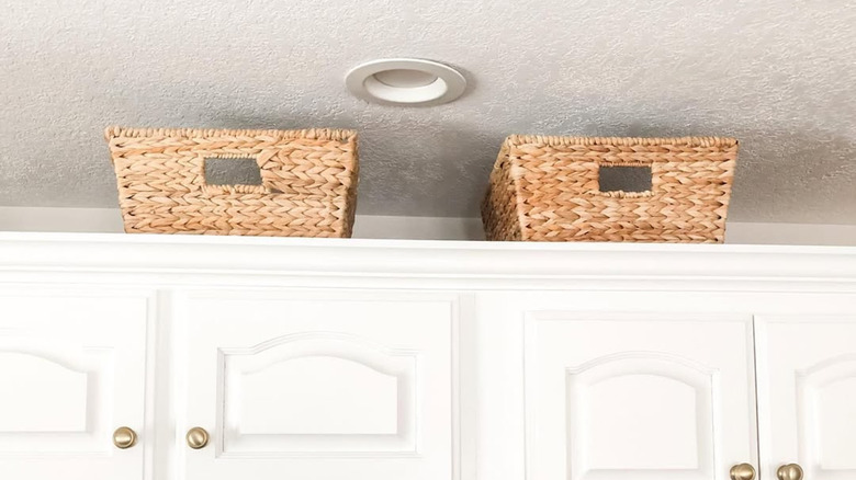 Two woven baskets on top of white kitchen cabinets