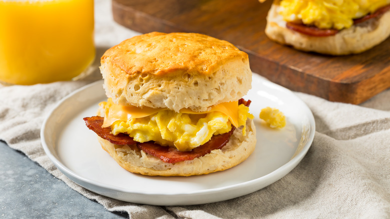 Breakfast sandwich featuring a biscuit, meat, eggs, and cheese on a white plate