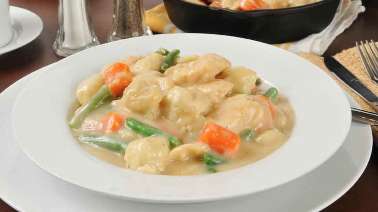 A bowl of chicken and dumplings with green beans and carrots