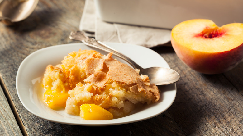 Homemade peach cobbler next to a halved peach on a wooden surface
