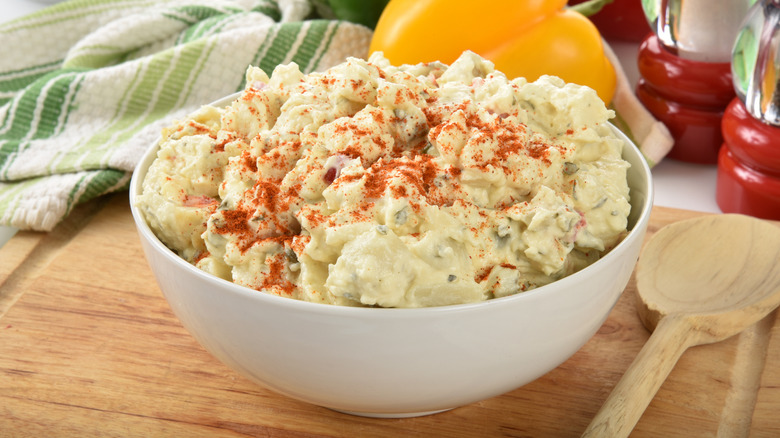 A white bowl of southern potato salad sprinkled with paprika