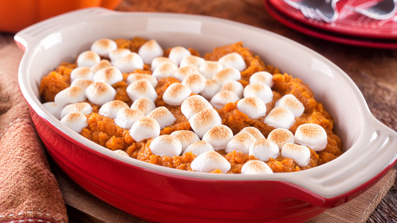 A red casserole dish of sweet potato casserole topped with marshmallows