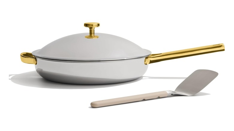 A shiny stainless steel Always Pan with gold-colored handles, and a spatula