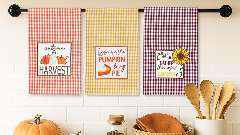 Three bright tea towels hang on a bar above a crowded kitchen surface