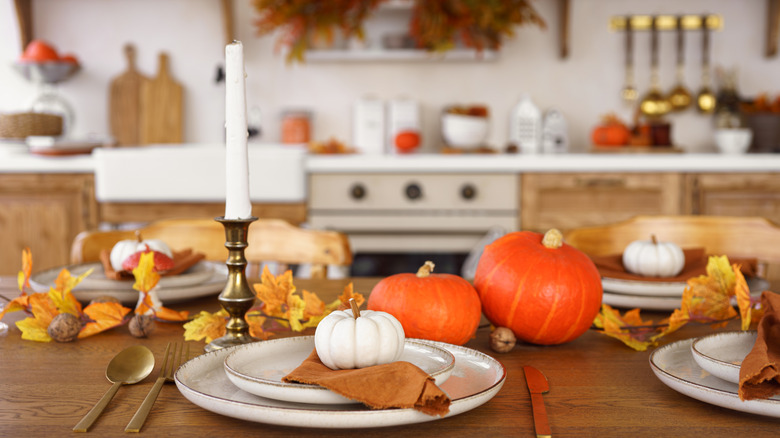 A festive Thanksgiving kitchen, with a decorated table with plates, candles and pumpkins