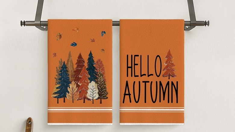 Two orange, autumn-themed kitchen towels hanging above a kitchen counter