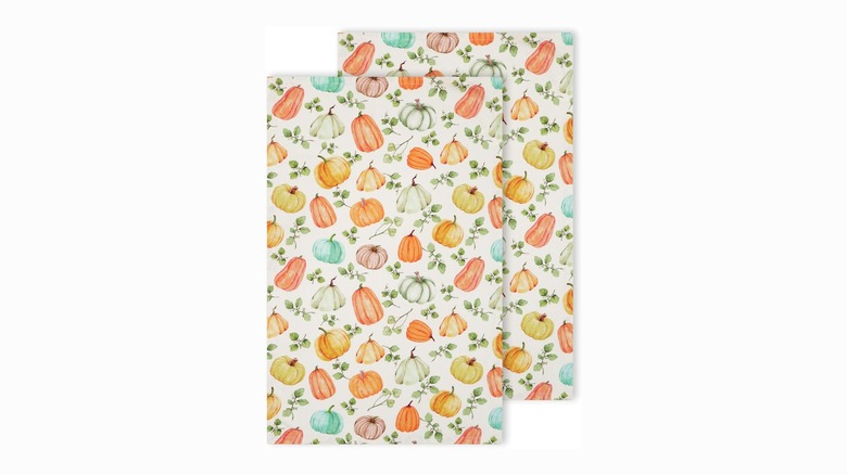 Two folded kitchen towels featuring colorful pumpkins and leaves on white backgrounds