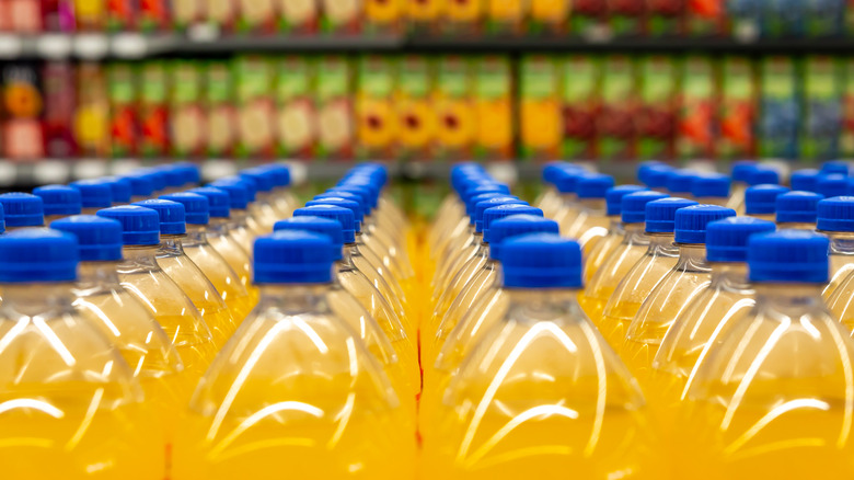 A row of soda bottles with orange liquid inside are displayed in a supermarket