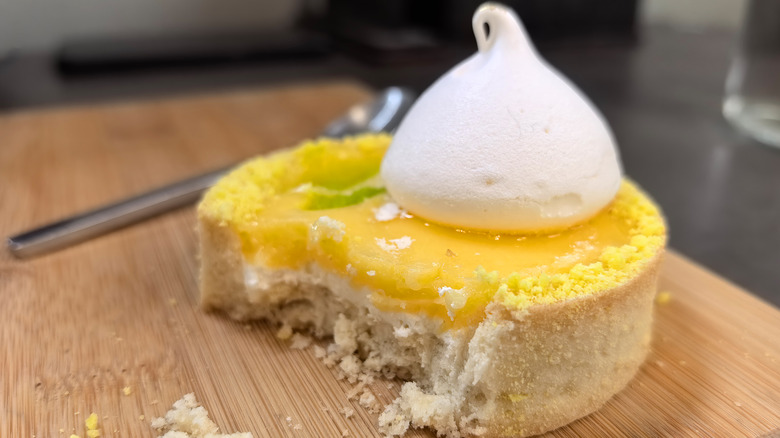Half-eaten lemon meringue tart on a wooden board
