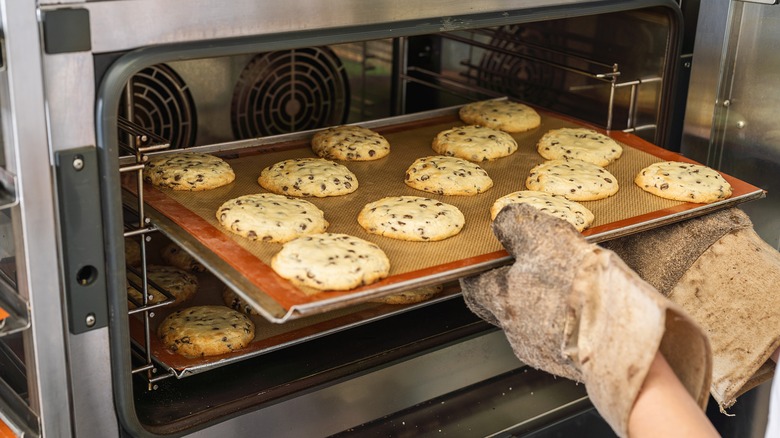 A person taking a tray of chocolate chip cookies out of an oven