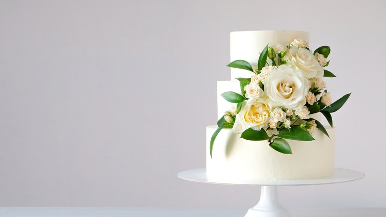A three tiered white wedding cake with flowers on a white cake stand