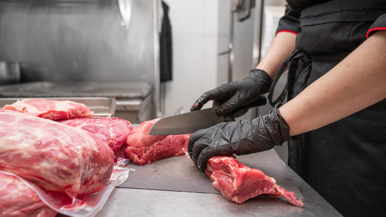 A meat cutter slices meat with a knife in a restaurant kitchen