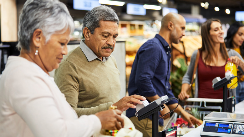 Several people standing in a checkout line at a grocery store