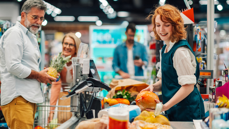 A man handing his groceries to the cashier at a grocery store checkout