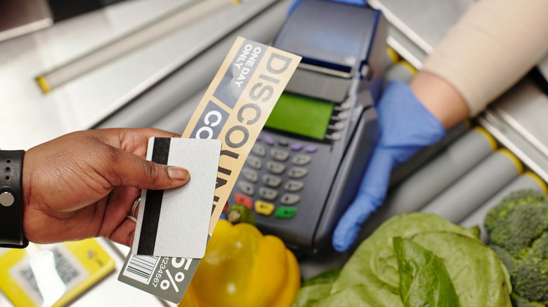 A person handing a discount coupon and their card to the cashier at a grocery store