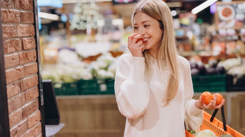 A woman trying to taste a tomato at a grocery store