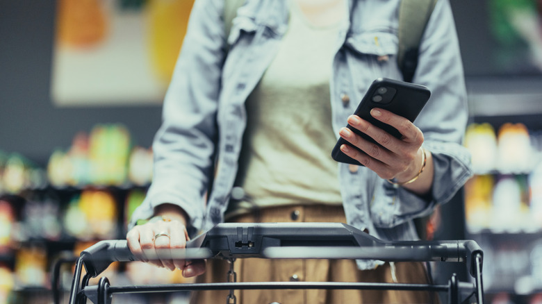 A woman using her phone while pushing a cart in a grocery store