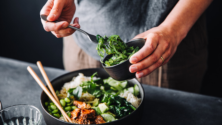 Man making bowl with rice, seaweed salad, edamame