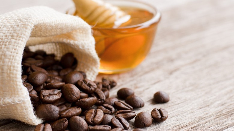 A white bag with coffee beans spilling out and a jar of honey in the background