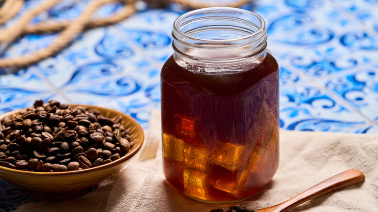Coffee cold brew steeping in a mason jar next to a bowl of whole coffee beans