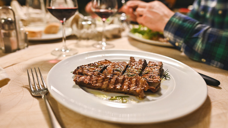 Sliced steaks sit on a plate in a steakhouse, as people dine in the background