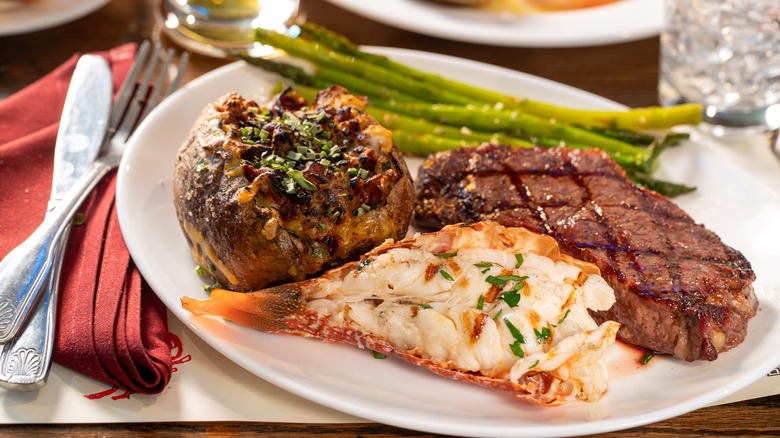 Steak, baked potato, lobster tail, and asparagus on a plate in a steakhouse