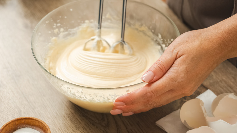 Using an electric beater in a glass mixing bowl full of cream-colored batter