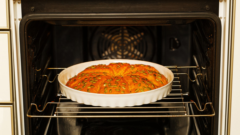 A pumpkin bread with pumpkin seeds on top in a white baking dish in the oven