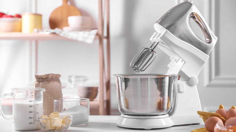 A white and silver stand mixer on a white counter with essential baking ingredients