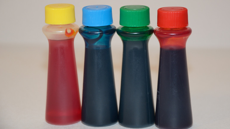 Four bottles of food coloring lined up against a white background