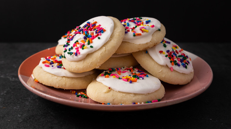 A pink plate filled with iced sugar cookies covered in sprinkles against a black background