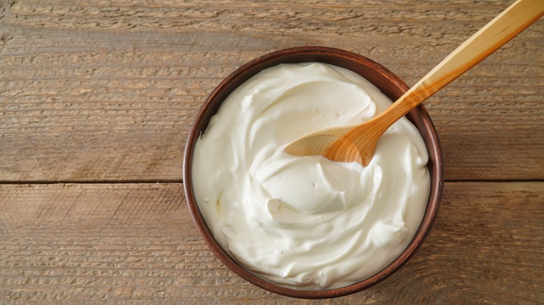 Sour cream in a bowl with a wooden spoon on a wooden table
