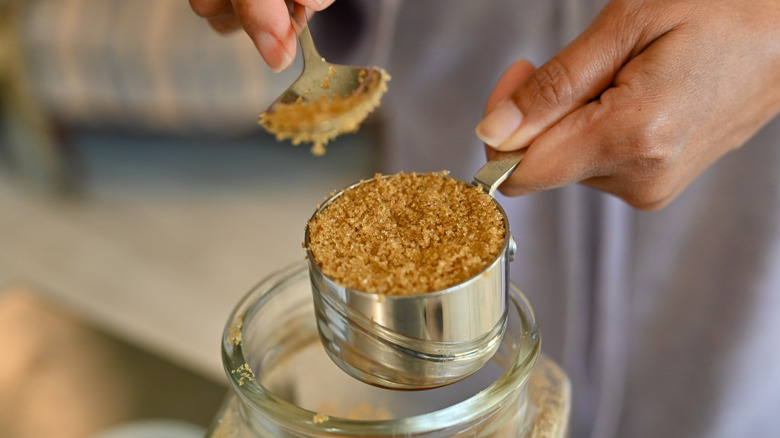 A person tapping down brown sugar in a measuring cup