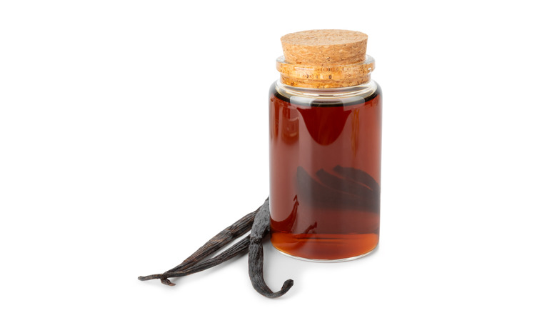 A bottle of vanilla extract next to vanilla beans on a white background