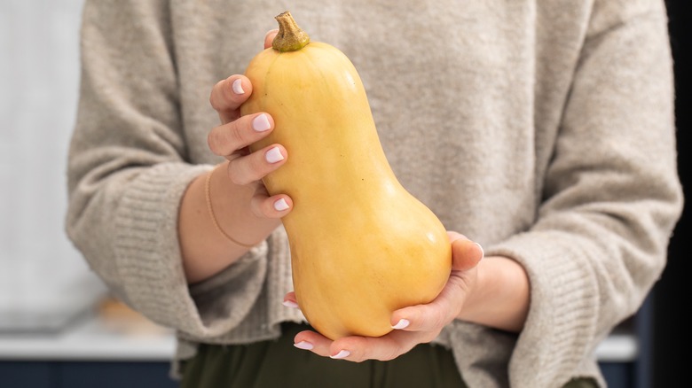 A person wearing a sweater and holding a butternut squash