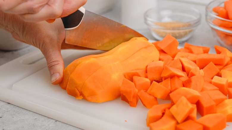 A person cuts chunks of butternut squash soup on a white cutting board