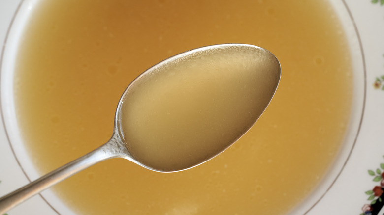 Close-up of chicken broth on a metal spoon above a bowl of more liquid