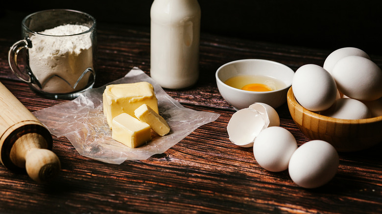 Flour, eggs, butter, and milk on a wooden surface with a rolling pin