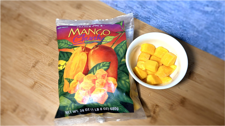 A bowl of mango chunks next to an unopened bag, on a table