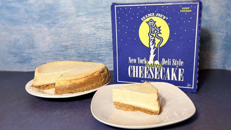 A slice taken from a large cheesecake, on a plate, in front of its packaging