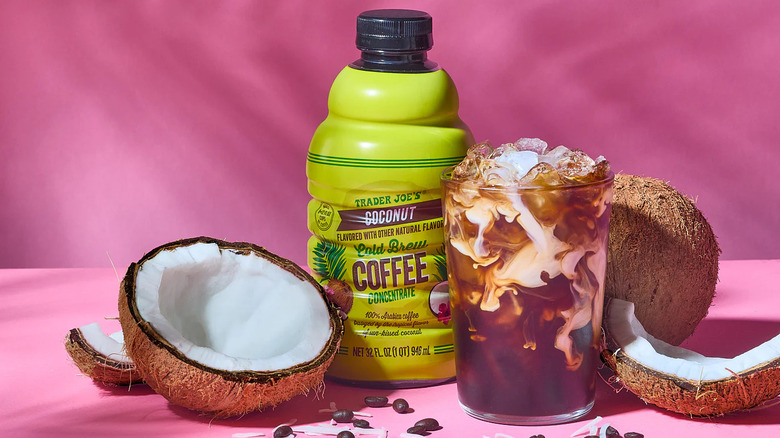 Coconut cold brew concentrate in a lime green bottle with coconuts and coffee glass against a pink background.