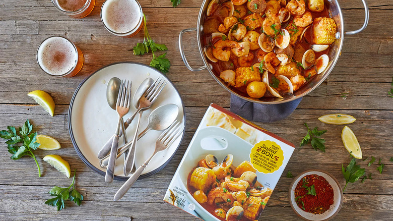 An overview photo of a seafood boil in pot with plate with forks and spoons nearby as well as the box, garnishes of parsley and lemon, and pints of beer.