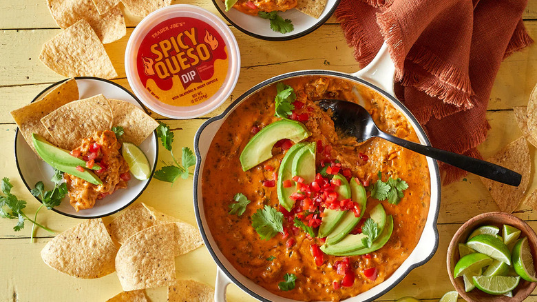 Spicy queso dip in pot with chips and limes with the spicy queso container nearby.