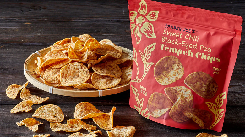 Sweet chili tempeh chips on plate with the red bag on a wooden table.