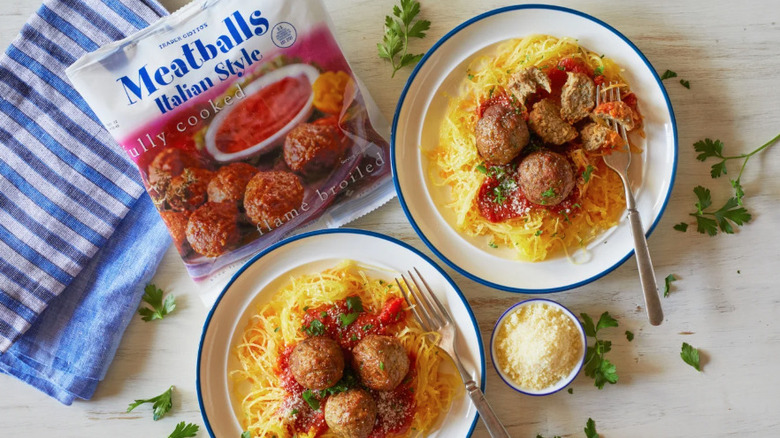 Package of Trader Joes Frozen Italian-style meatballs next to two bowls of spaghetti and meatballs
